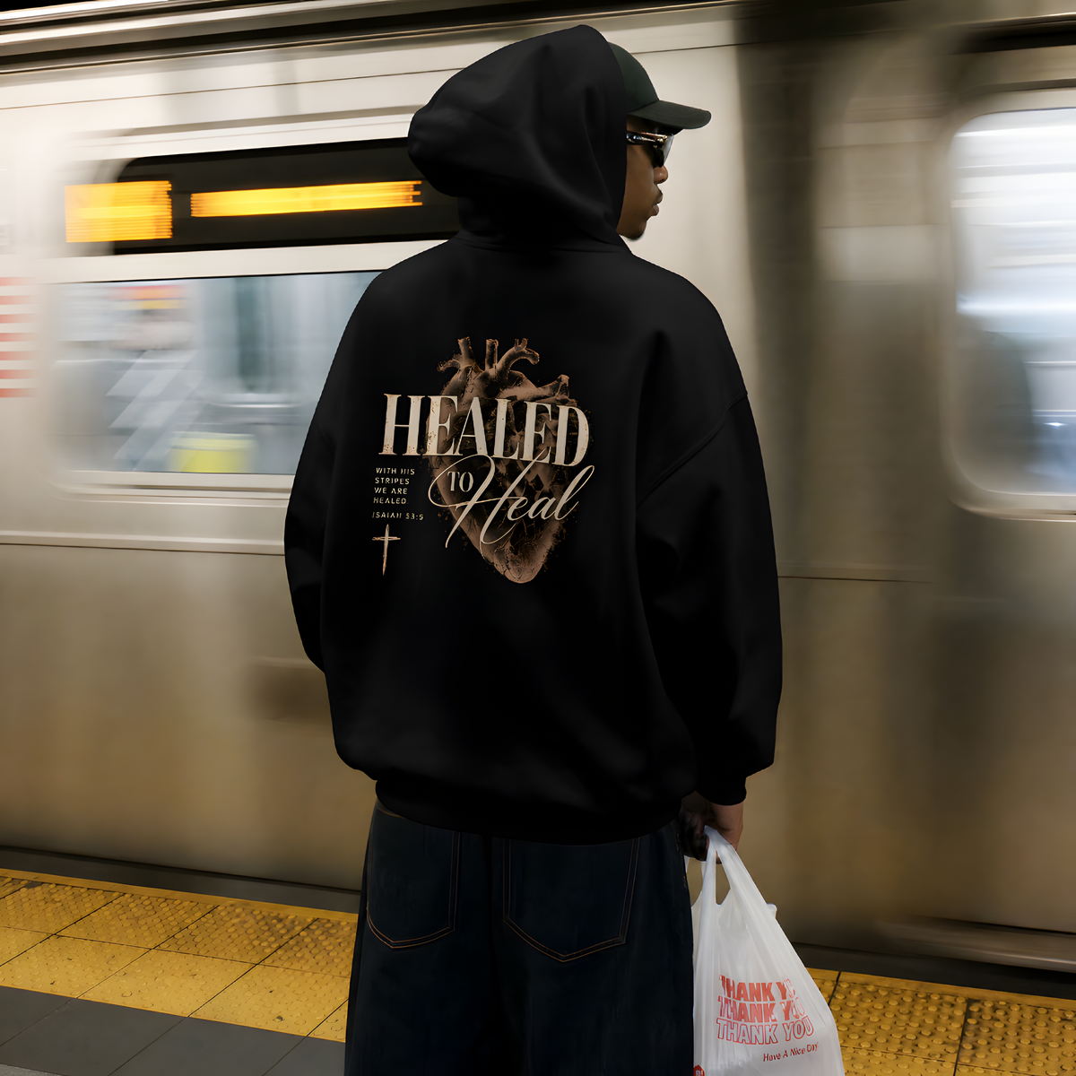 Back of the black Healed to Heal hoodie: anatomical heart and Isaiah 53:5 print, worn on a subway platform