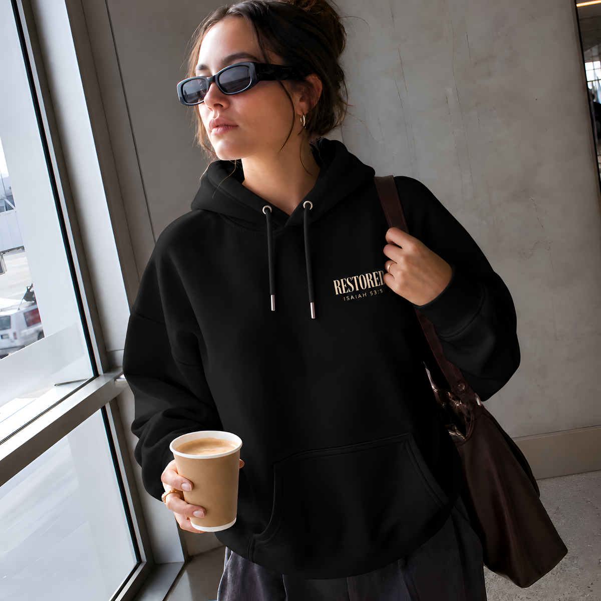 Woman wearing the black RESTORED Isaiah 53:5 hoodie by a window